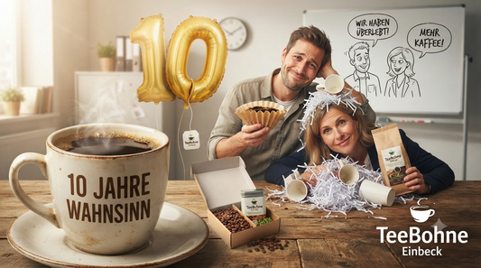 Kollegen feiern ein 10-jähriges Firmenjubiläum mit einer großen Tasse Kaffee, einer Glückwunschkarte und einem Geschenkset von TeeBohne Einbeck vor einer geschmückten Wand