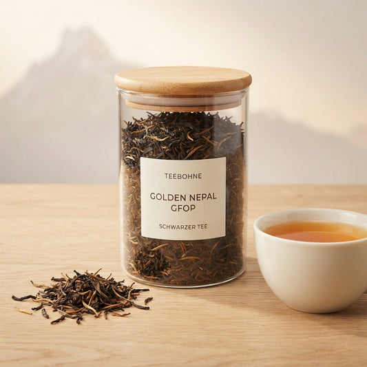 TeeBohne: Eine transparente Glasteedose mit Holzdeckel, gefüllt mit losem Golden Nepal GFOP Schwarztee, steht auf einer natürlichen Holzoberfläche. Auf dem cremefarbenen Etikett ist "TEEBOHNE GOLDEN NEPAL GFOP SCHWARZER TEE" zu lesen. Neben der Dose liegt eine kleine Menge des Tees, die die feinen goldenen Blattspitzen zeigt, sowie eine weiße Teetasse mit einem gold- bis rotgoldenen Aufguss. Die Atmosphäre ist dezent, elegant und erinnert subtil an eine Himalaya-Kulisse